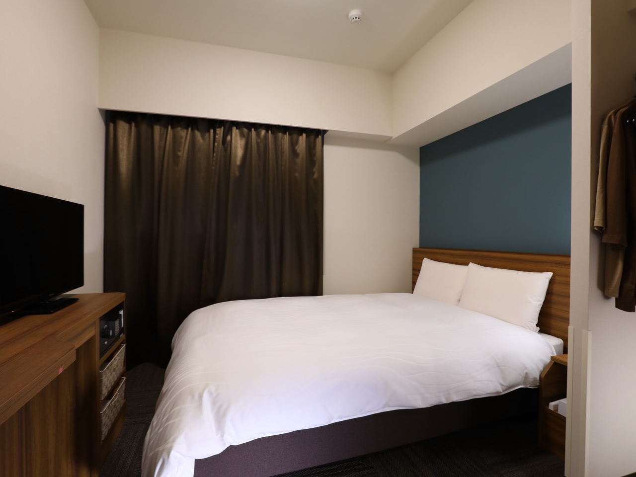 The Standard Double at Dormy Inn Ikebukuro: a double bed between a TV unit and a closet, with a dark curtain behind it.