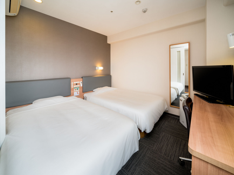 The Twin room at Super Hotel Anjo Station Front: two beds side by side along the far wall, a mirror, a TV and a desk on the right.