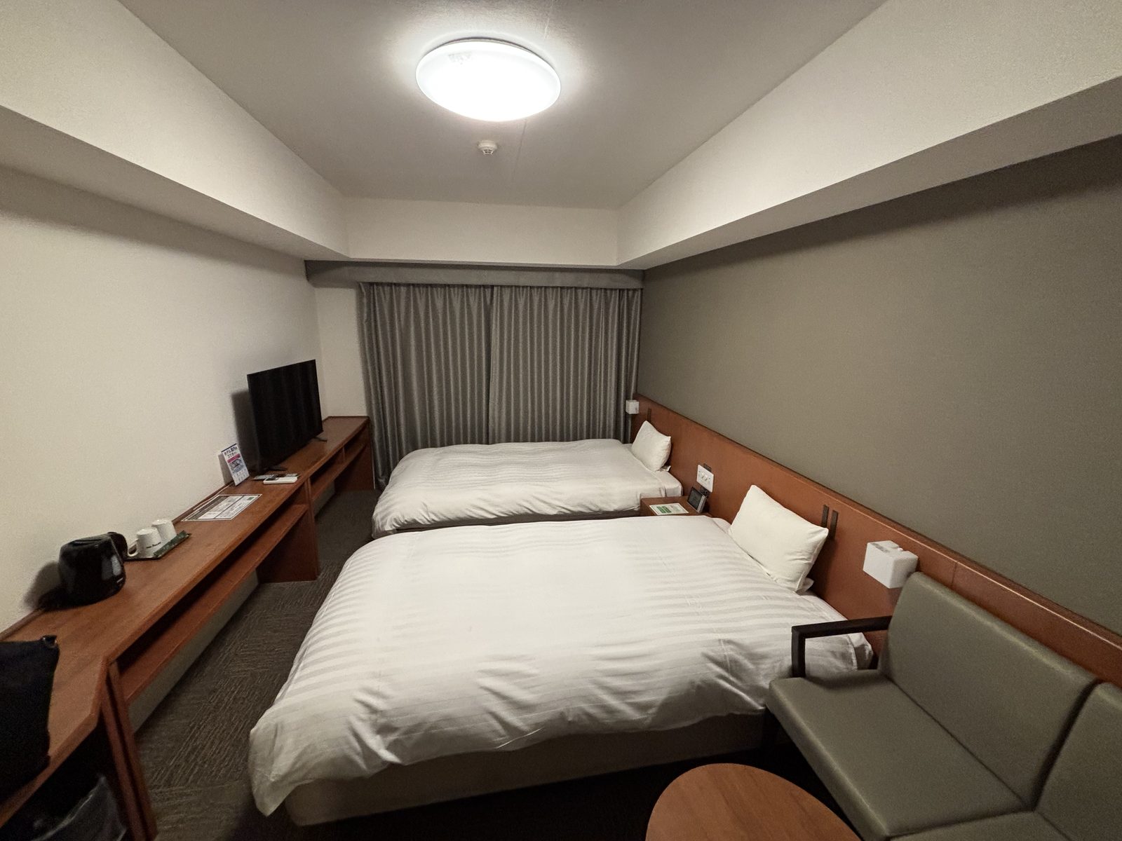 A narrow twin room with two beds side by side and a desk running the length of the opposite wall.