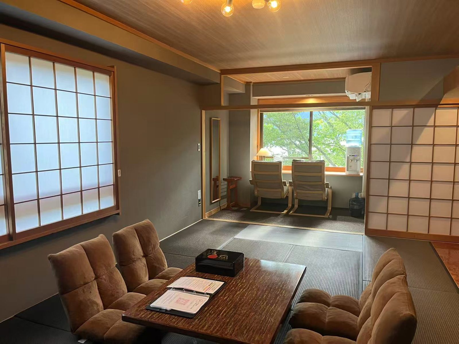 A tatami guest room in daylight, with a low table in the middle, floor chairs around it, and a wide window bay beyond.
