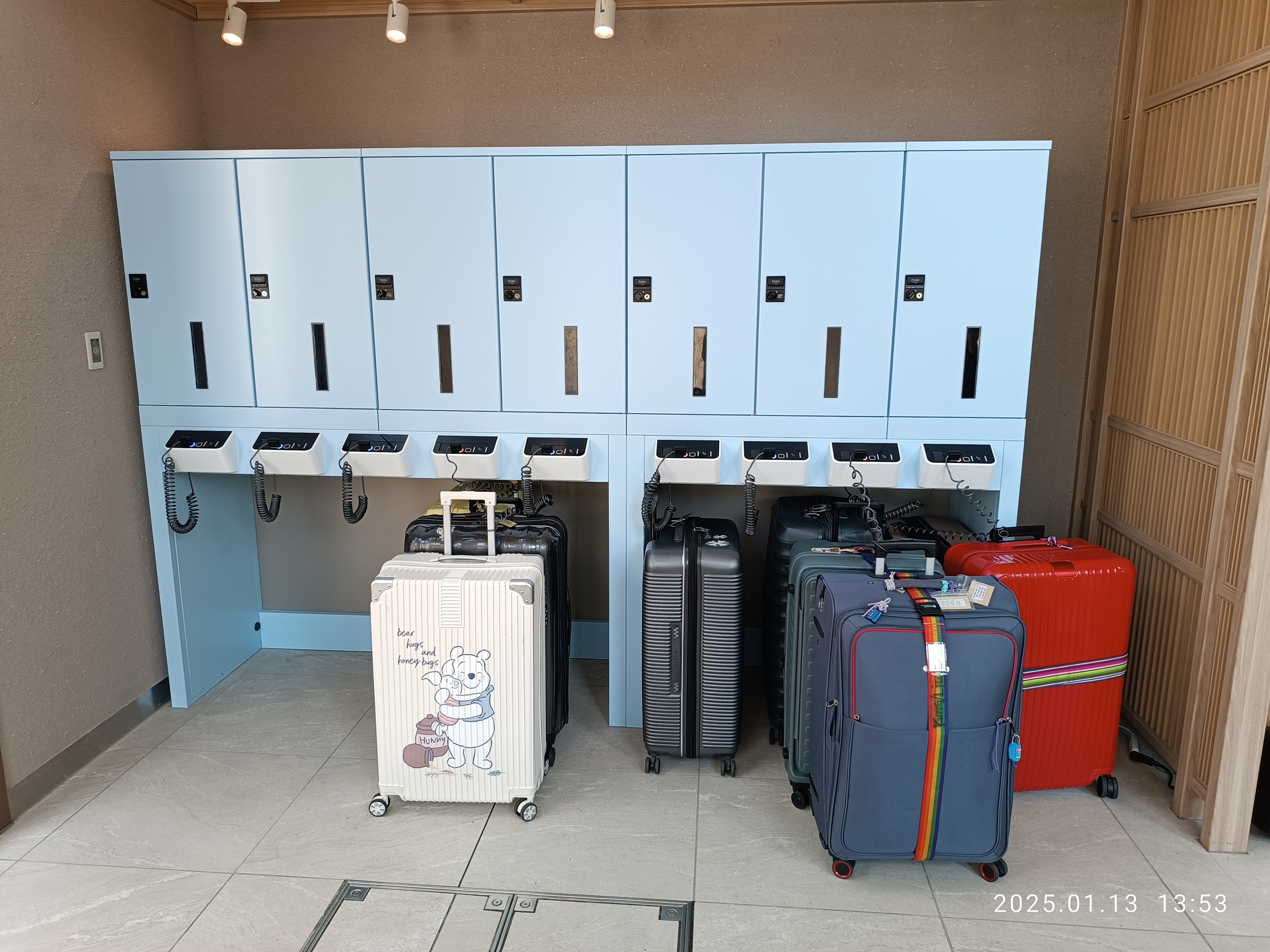 A hotel luggage storage area: blue lockers with charging cradles above, and seven suitcases of different colors standing in front.