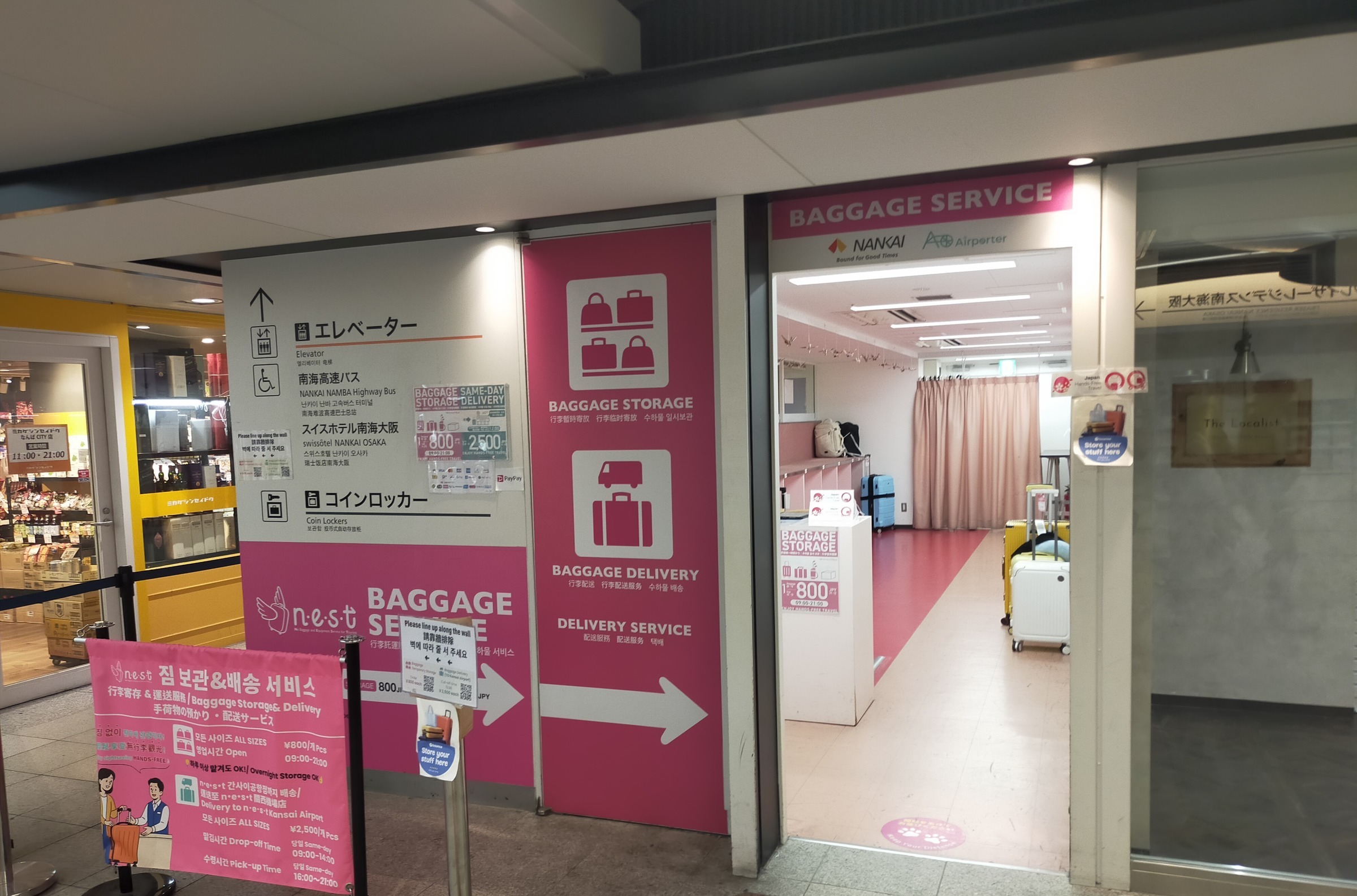 The entrance to a baggage storage and baggage delivery service in a Japanese railway station, with pink signs and suitcases visible inside.