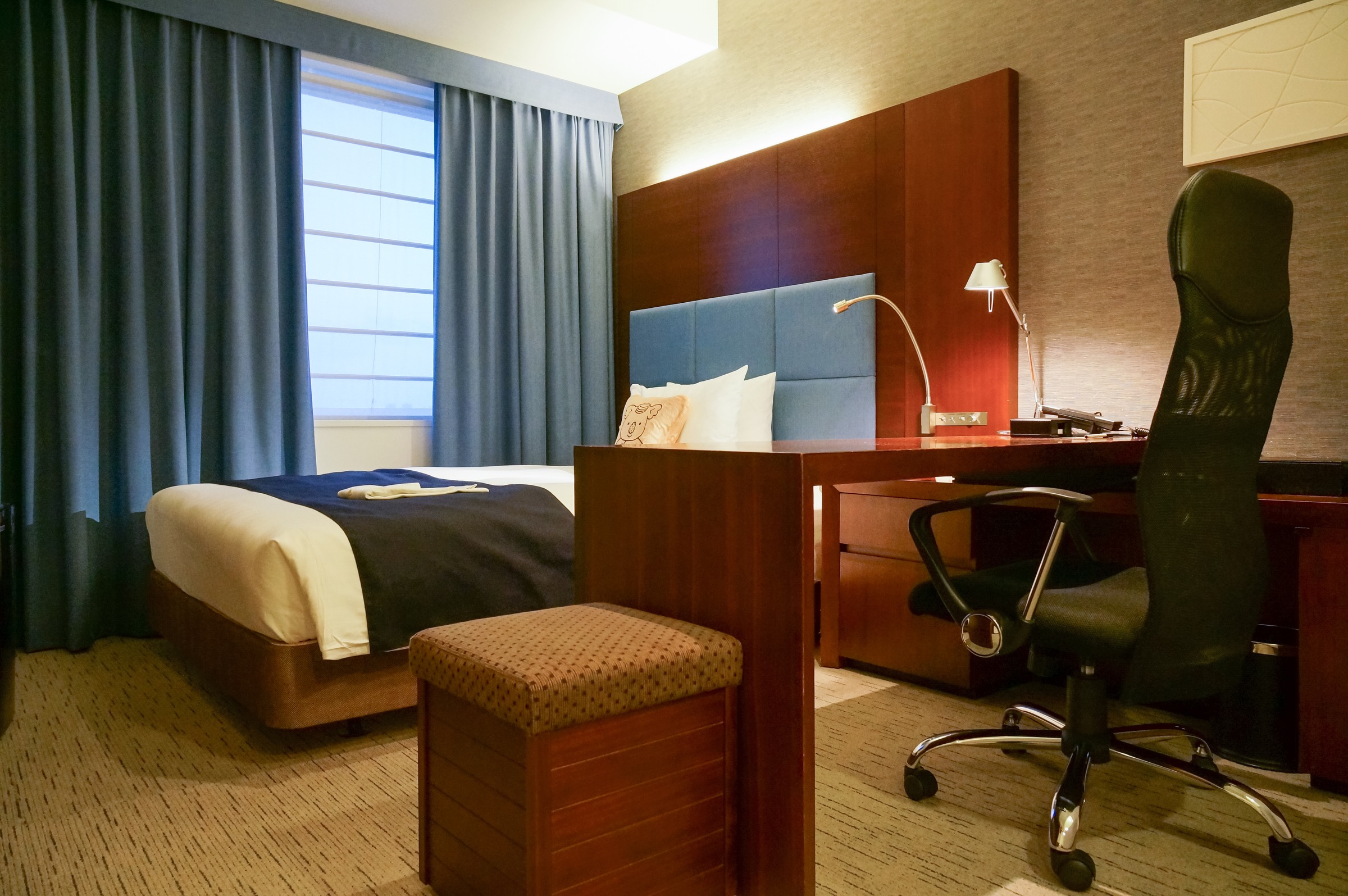 A business hotel single room with a bed by a window, a wood desk and an office chair.